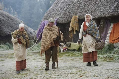 Guides dressed in traditional highland clothes walk past the thatched cottages of the Highland Folk Museum