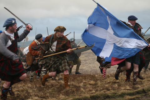 Highlanders dressed in kilts and carrying swords recreate a charge during the Battle of Culloden