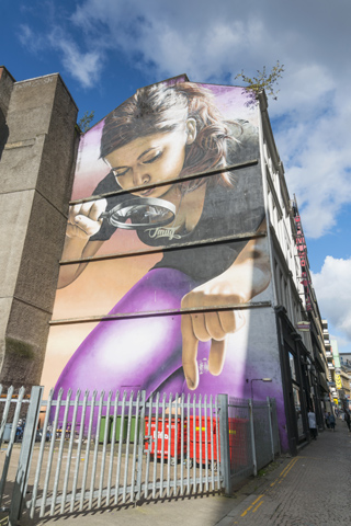Mural painting of a woman with a magnifying glass trying to pick something up from the ground