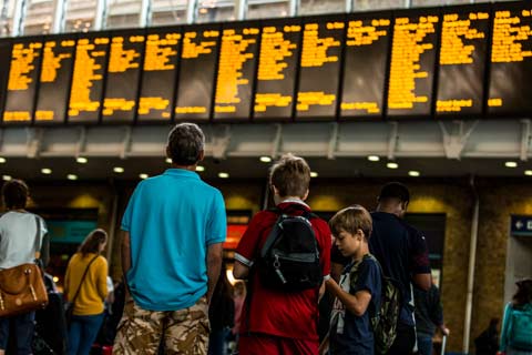 A man studies the destination board at the station while his two boys play on their phones