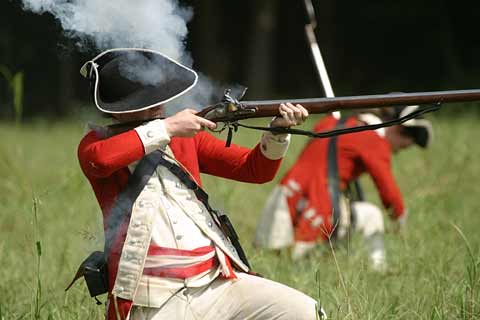 Redcoat soldier kneels as he fires a shotgun