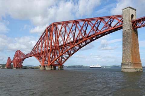 A cruise ship sits under the red painted Forth Rail Bridge
