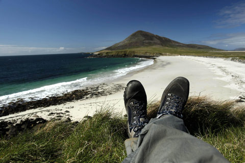 A walker rests at Northton beach, looking towards the hill of Ceapabhal on the Isle of Harris