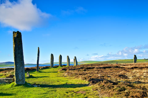 Seven standing stones of the Ring of Brodgar on Orkney under a bright blue sky with Loch Harray in the distance 