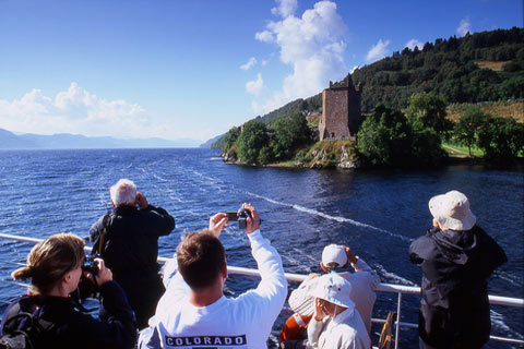 Group of passengers on Loch Ness Ferry Cruise taking photographs of a castle on the shore