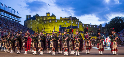 Bagpipers with audience on left and right and Edinburgh Castle in background at Edinburgh Tattoo in evening