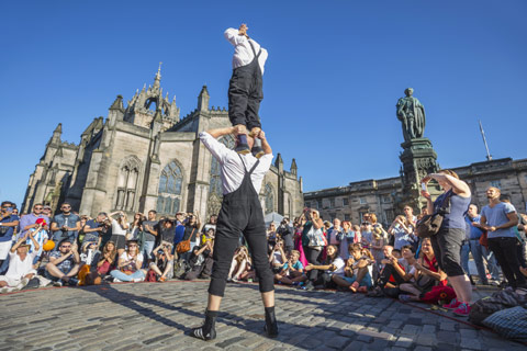 male street performer with man on his shoulders surrounded by audience during Edinburgh Fringe