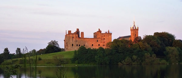 ruins of Linlithgow Palace at sunset next to Linlithgow Loch and partly obscured by trees