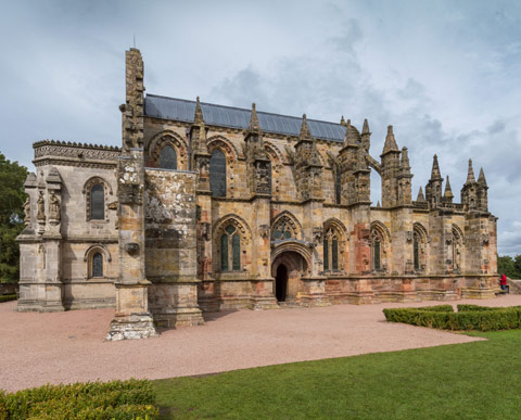 Rosslyn Chapel-  stone chapel with turrets and arched windows with gardens in foreground