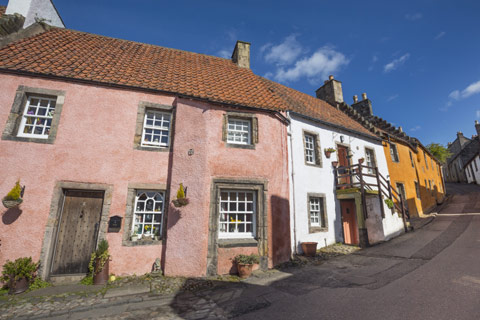street winding uphill with pink, white and yellow cottages on a bright day