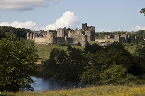 The turrets and defensive walls of Alnwick Castle seen across the River Aln