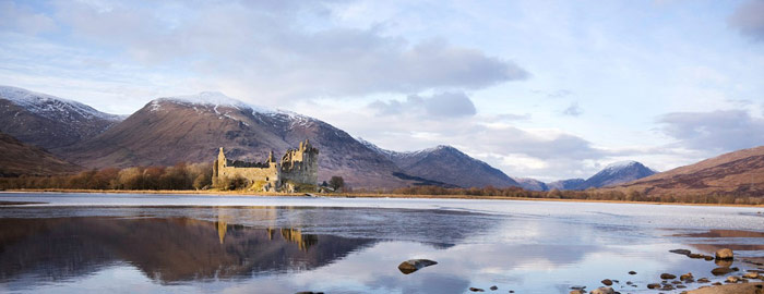 Kilchurn Castle - sand coloured ruined castle on banks of calm loch with snowy mountain peaks in background