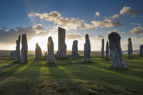 The sun rises through the Callanish Standing Stones on a bright summer day
