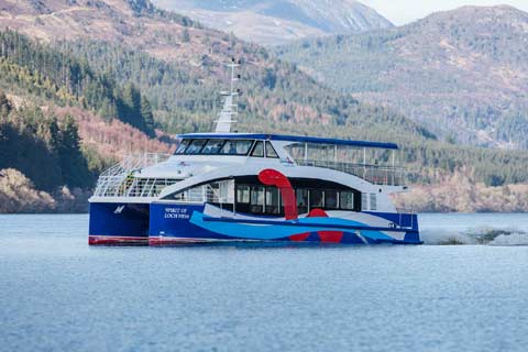 The brightly painted Spirit of Loch Ness cruise boat sailing on the Loch with tree-covered hills in the background