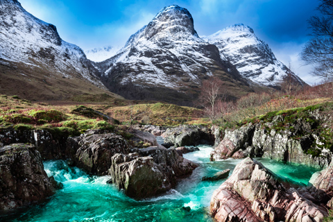 Snow capped mountains of Glen Coe overlook the tumbling turquoise water of the River Coe