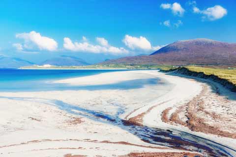 The white sands of Luskentyre Beach extend towards a heather clad hill