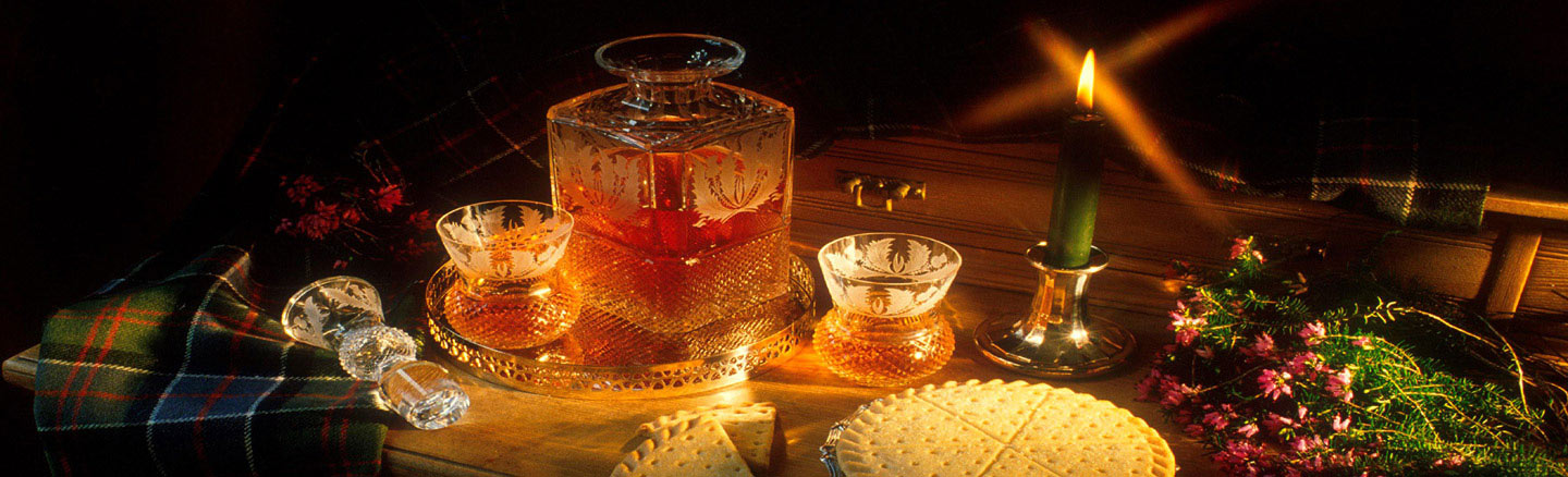 A whisky decanter and two glasses sit on a candle-lit table dressed with tartan