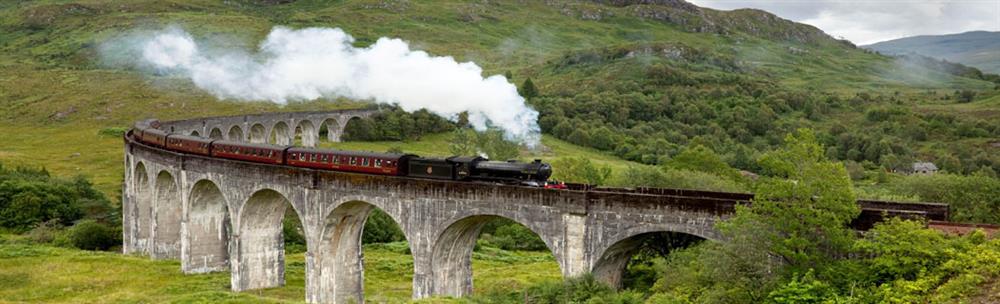 The black engine and red carriages of the Jacobite Steam Train cross the Harry Potter bridge