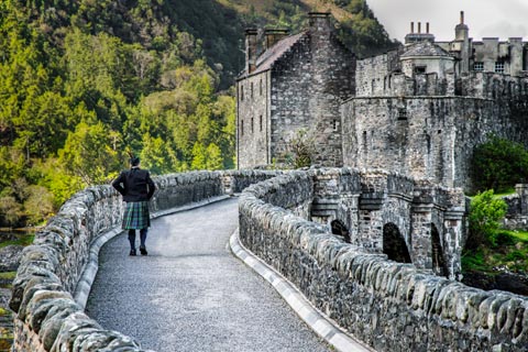 Kilted man walking over the bridge at Eilean Donan Castle
