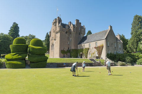 group of people playing croquet in front of intricately turreted Crathes Castle and sculpted hedges