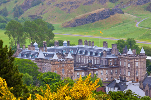 looking down on to Holyrood Palacewith yellow flag flying and hill of Arthur's seat in background