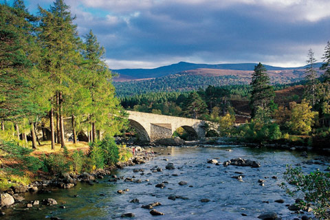 white stone bridge crossing river with dramatic mountains in background in Cairngorms National Park