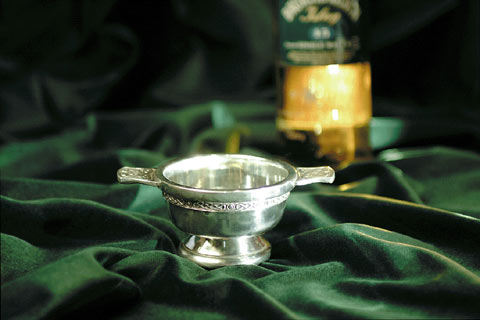 Shining silver quaich in foreground with whisky bottle in background