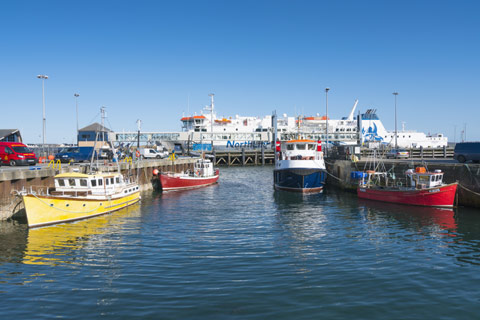 colourful boats in water and a large ferry at a terminal