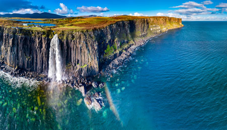 Kilt Rock - sea cliff with distictive pleats in the rock in bright blue water with white waterfall