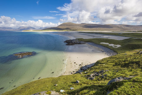 clear blue water and white sandy beach with mountains in background in Outer Hebrides