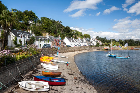 colourful rowing boats on beach with pretty white houses in background in Plockton